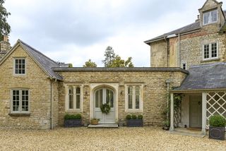 exterior of cotswold stone home with extension and arched double front door with christmas wreath
