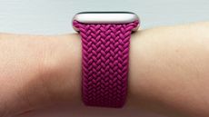 A side view of the magenta-colored Apple Braided Solo Loop attached to a light pink Apple Watch on a woman's wrist.