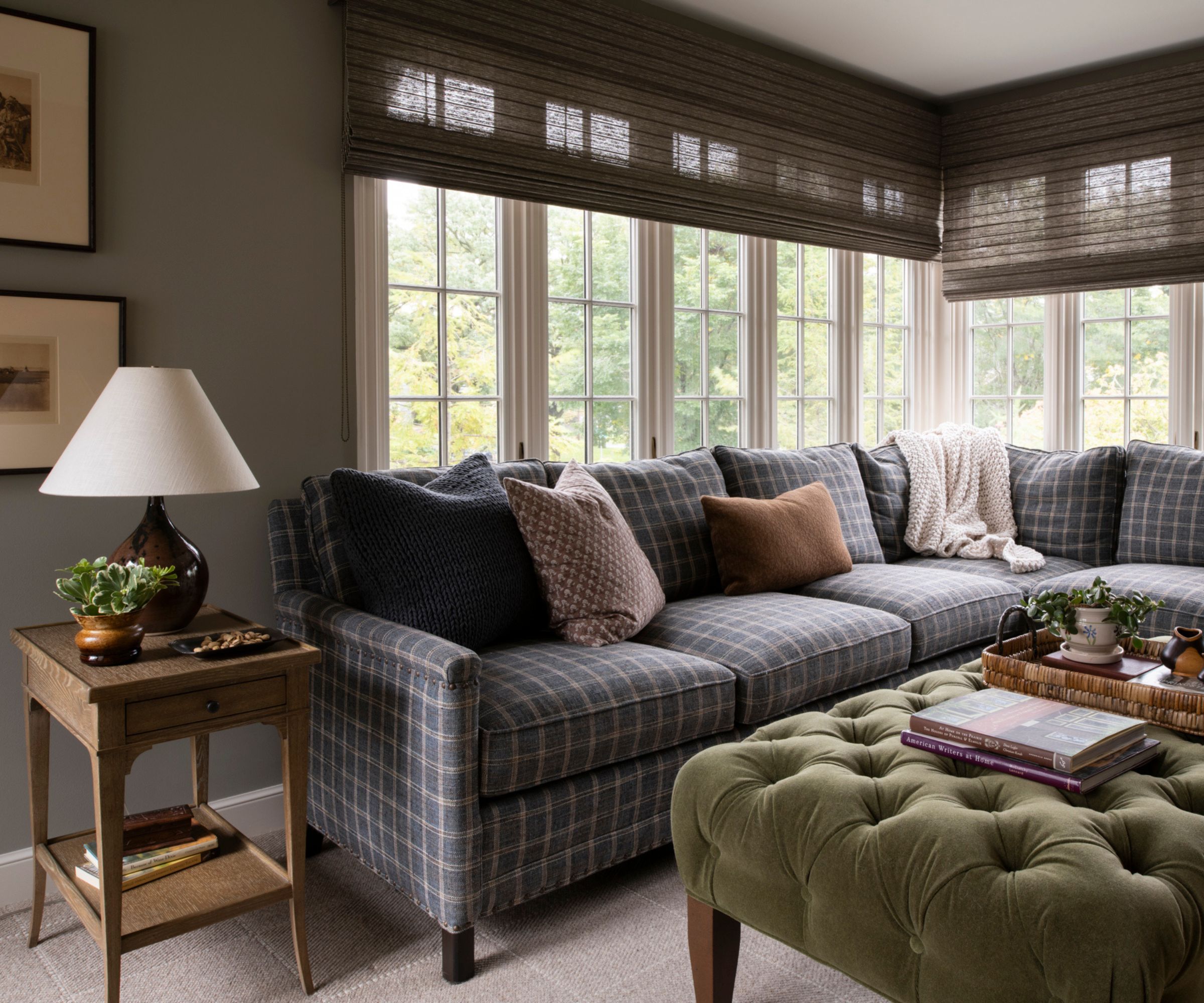 neutral snug room with large windows and a blue plaid corner sofa with a green velvet ottoman and vintage style decor