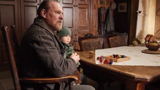 Tony Pitts as Richard Alderson sits at a table holding baby Jimmy in the All Creatures Great and Small Christmas Special 2024.