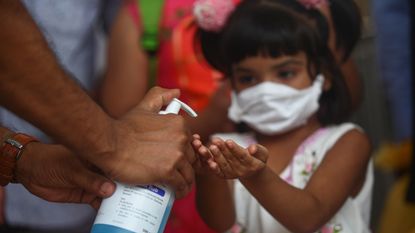 A child in Bangladesh receives a squirt of hand sanitizer to ward off COVID-19 in a March 2020 photo. There's been a sharp uptick in chemical burns from sanitizer to children's eyes since the start of the pandemic, largely due to public dispensers.