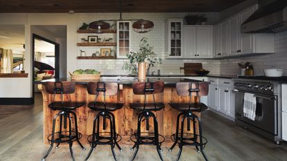 kitchen with wooden island, wood and metal bar stools, industrial style light and white cabinets and backsplash tiles