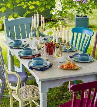 wooden outdoor dining table with mismatched chairs painted in pastel shades