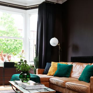 A black-painted living room with a brown leather sofa and black curtains covering a bay window