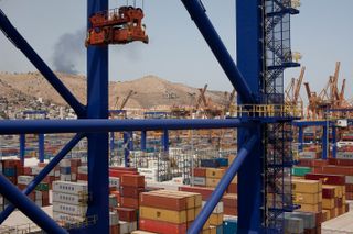 Smoke seen rising from a hill in the distance with a busy dockside container park in the foreground.