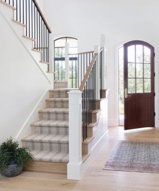 A home entryway with a plaid runner on the stairs and a wooden front door