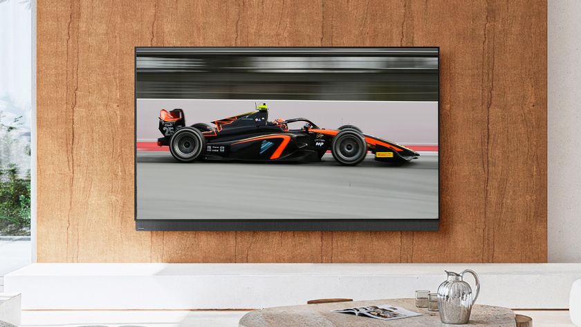 The Panasonic Z95B OLED TV mounted on a wall in an upscale living room setting. Its displaying the image of a Formula 1 race car in motion.