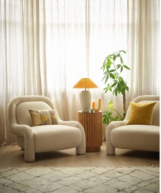 A light-filled seating area with a textured rug, boucle armchairs and a small plant