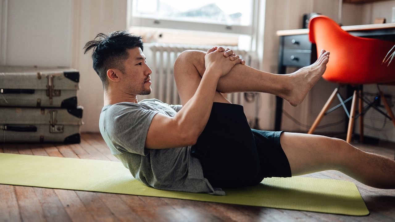 Young Asian man stretching during workout on exercise mat at home - stock photo