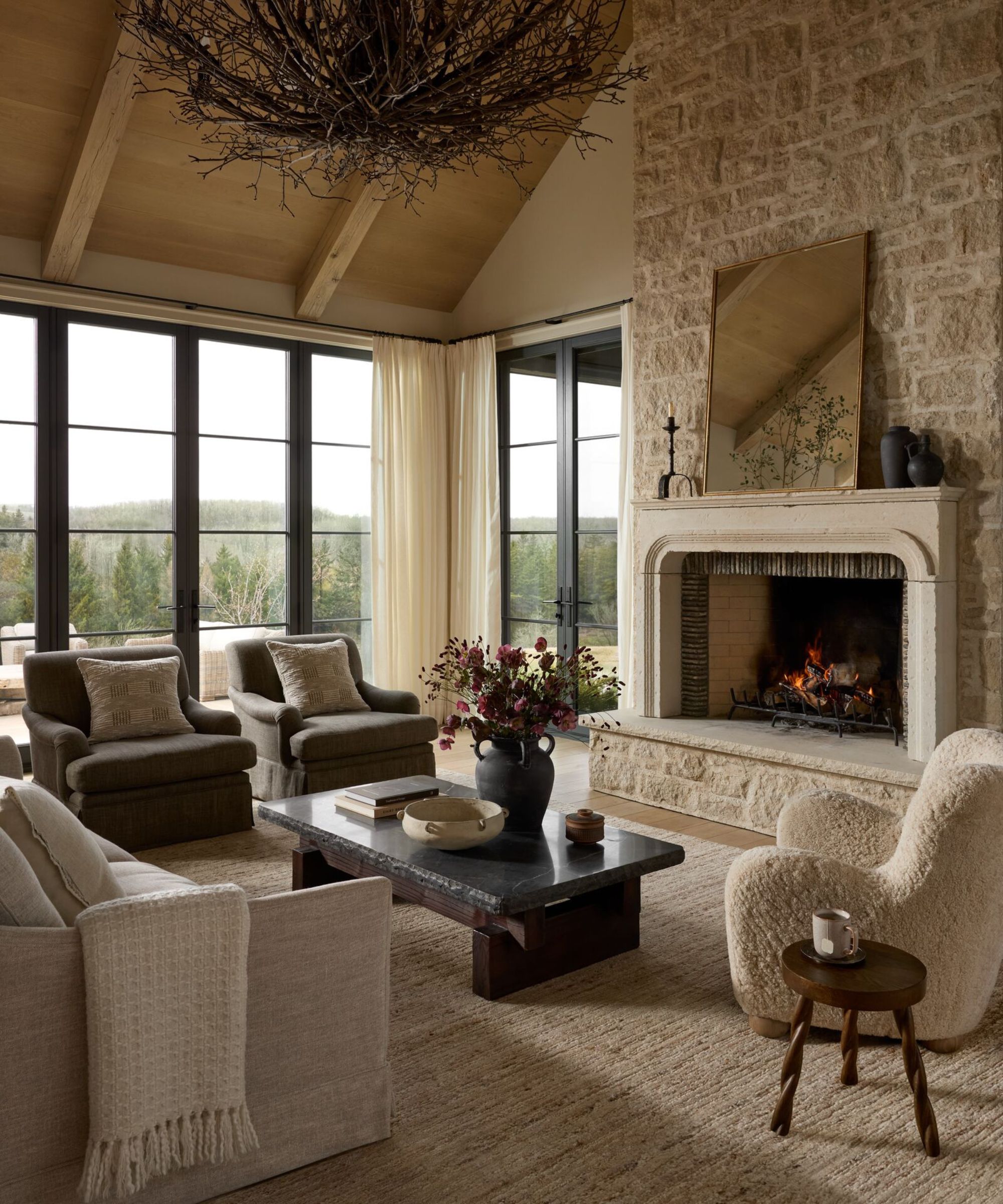 cozy living room scheme with a wooden pitched roof, stone neutral large fireplace, neutral sofa and a boucle armchair