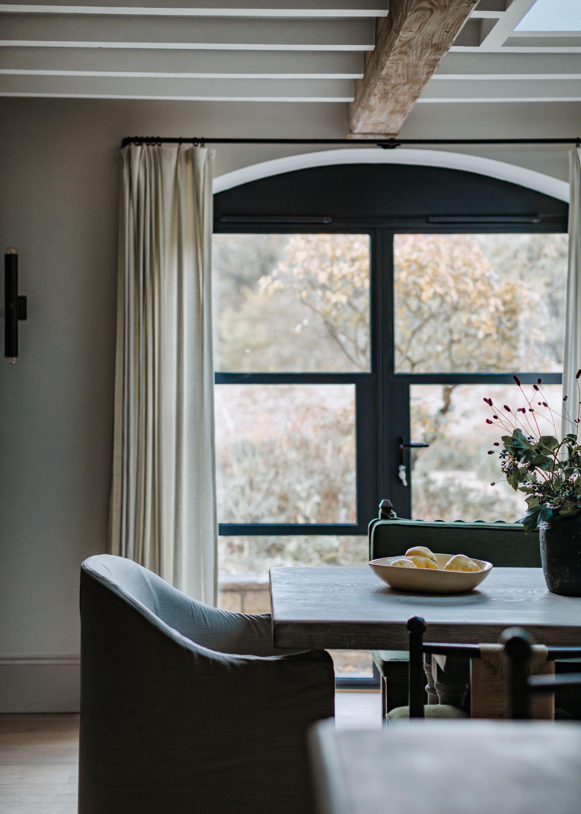 A dining room with black French doors with beige curtains.