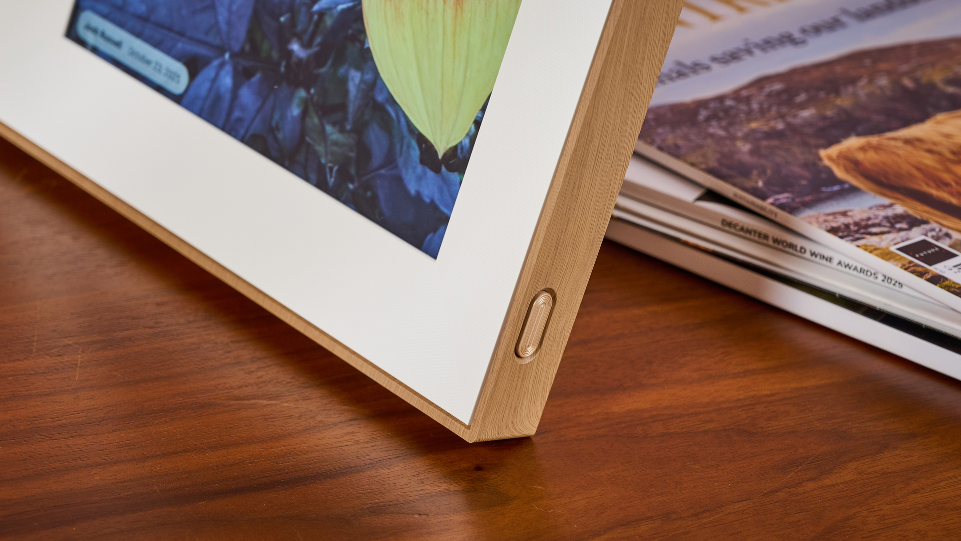 A closeup of the front corner of the Pexar Starlight 15.6-inch, showing the wood-grain frame and the power button.