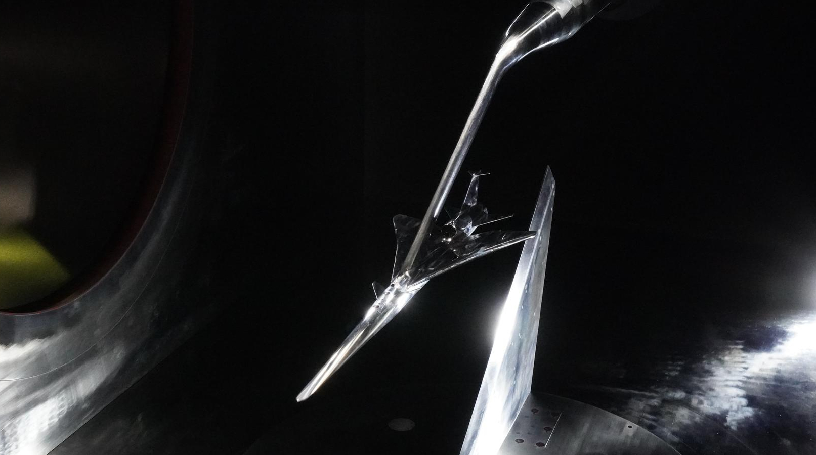 A metal model of a plane floats in a dark wind tunnel