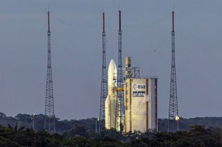 A dim grey sky sits behind the spotlit Ariane 5 standing at the luanchpad at Europe's Spaceport in French Guiana.