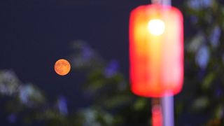 a large red lantern like feature on the right and a orange colored full moon on the left in the distance.