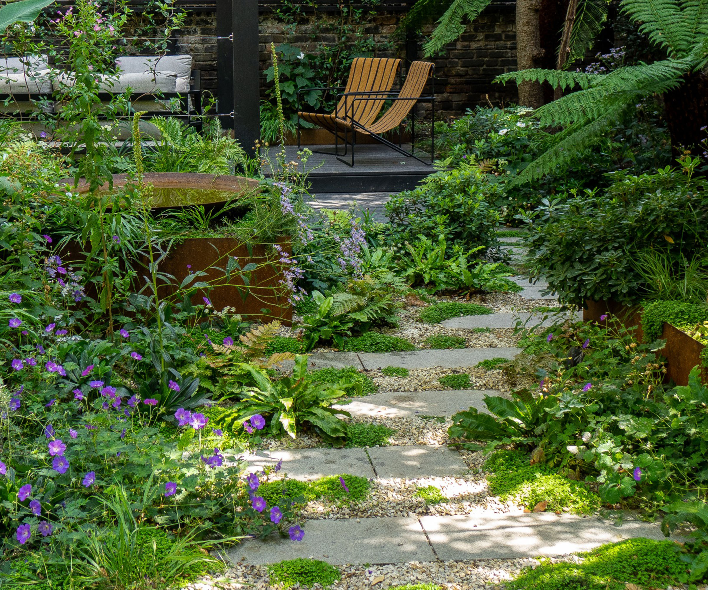 A small back garden with a seating area at the bottom and a permeable green pathway leading to it