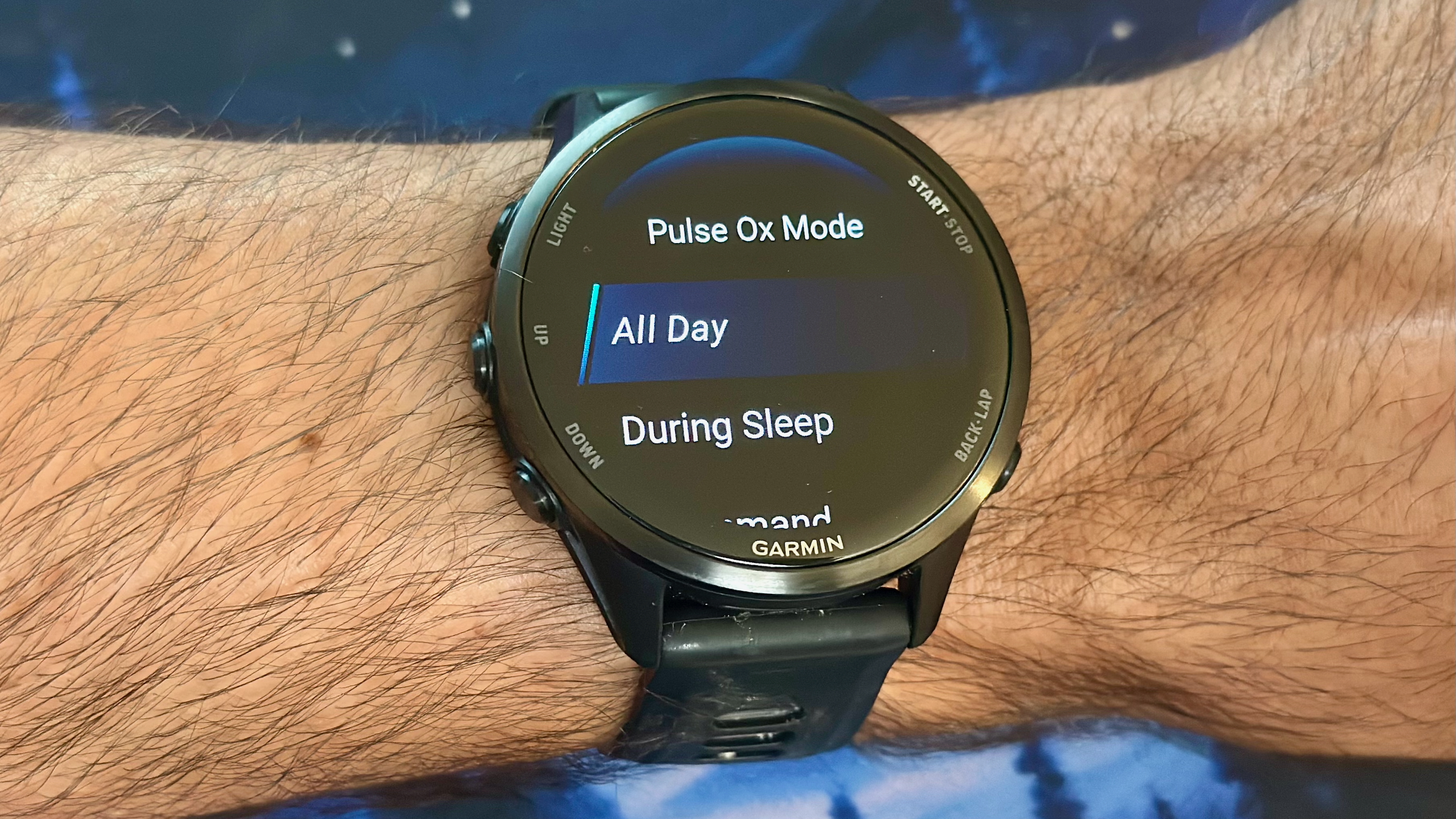 The Garmin Forerunner 970 on a wrist showing the Pulse Ox Mode menu, with &quot;All Day,&quot; &quot;During Sleep,&quot; and (cut off along the bottom) &quot;On Demand&quot; options available.