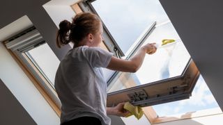A woman cleaning velux windows from the inside with a handheld squeegee tool