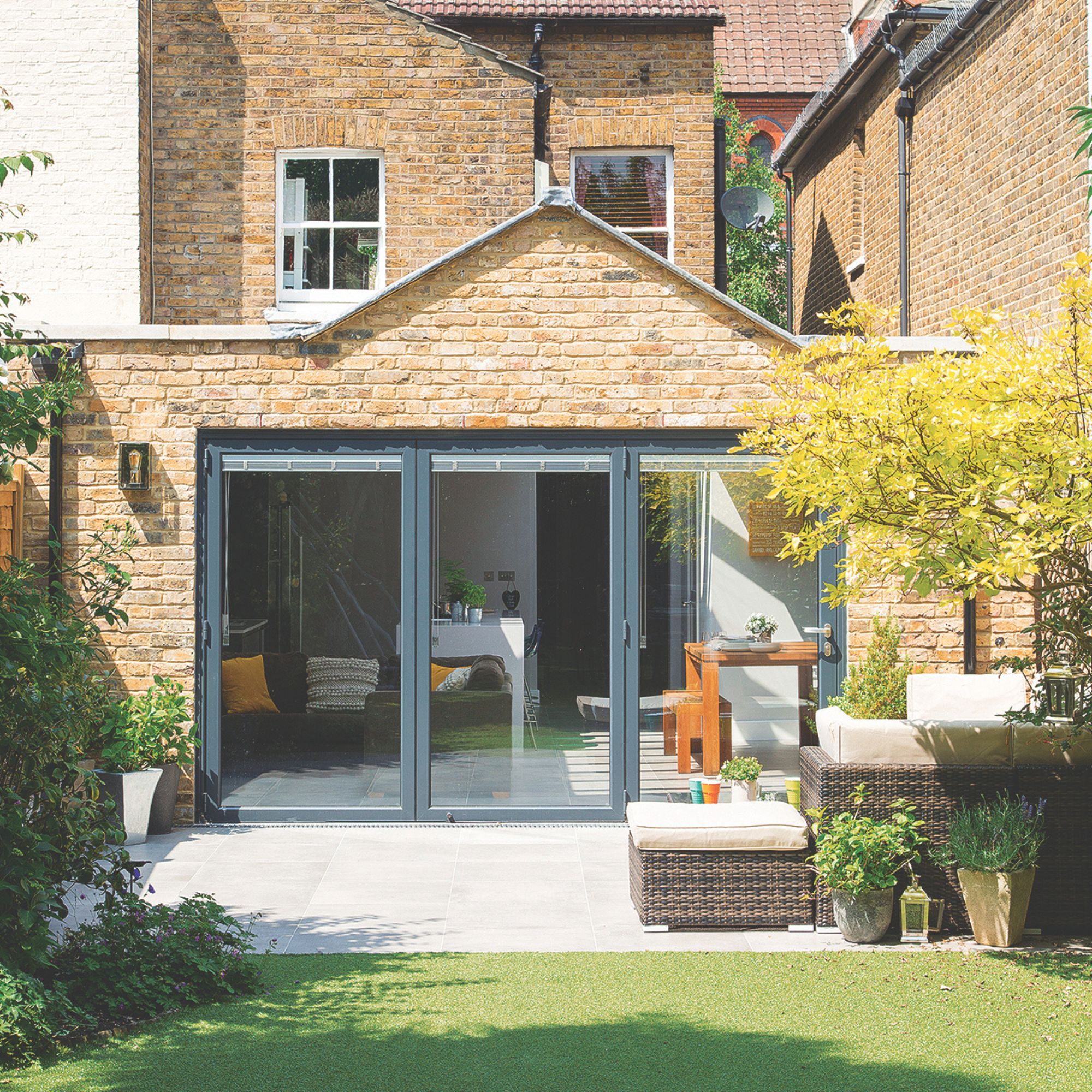 Porcelain tiled patio area in garden next to cut lawn with rattan garden furniture