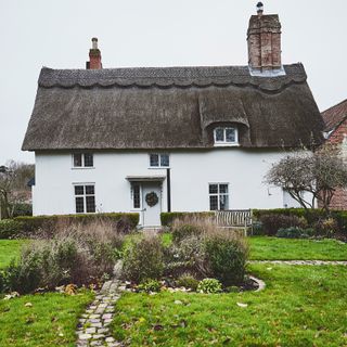 thatched cottage in winter with white walls with curving path leading to door with christmas wreath