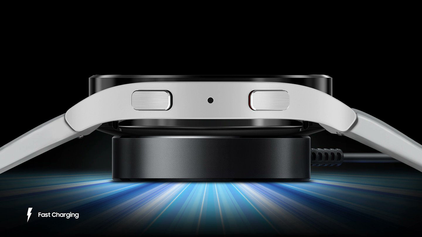 A render demonstrating a Samsung smartwatch charging on a wireless charger. The text 