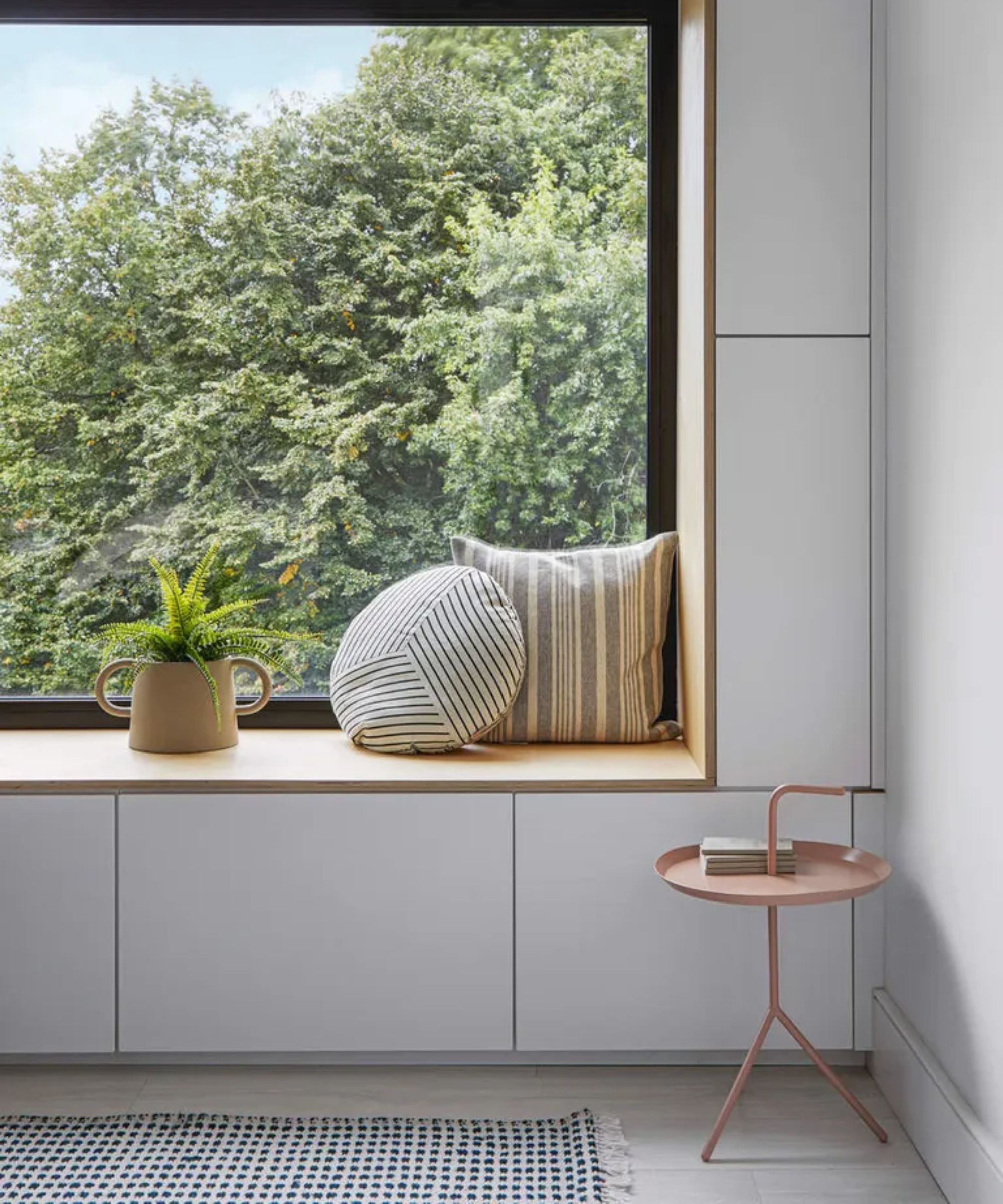 White cabinets around window seat, cushions, indoor plant