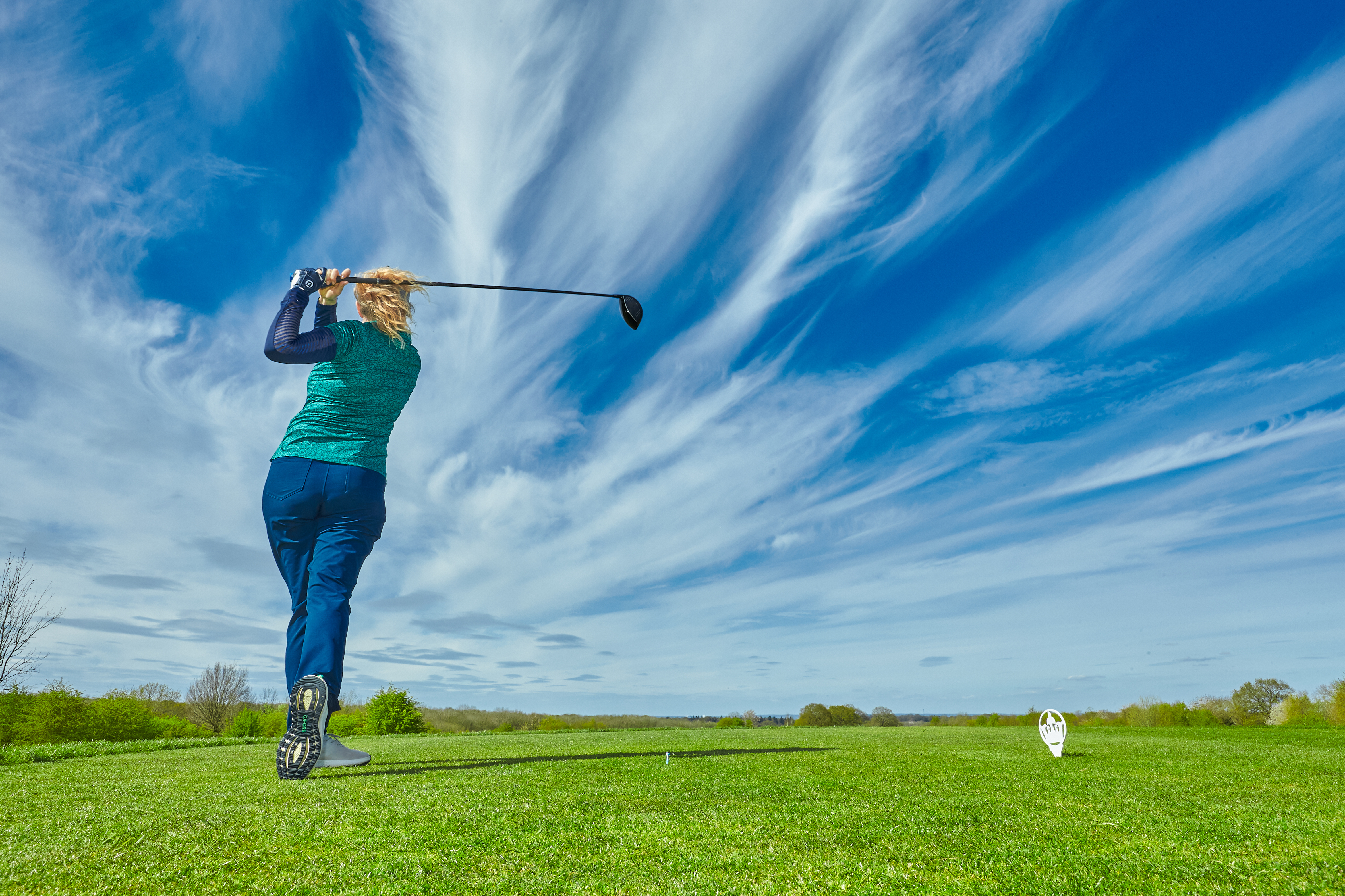 A golfer at the top of her backswing after hitting driver off the tee