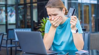 Mujer sorprendida por una estafa en línea, sosteniendo su tarjeta de crédito