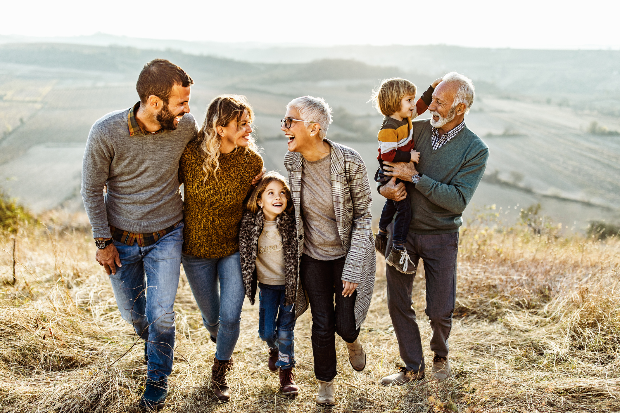 Happy extended family of many ages communicating while walking in autumn day on a hill.