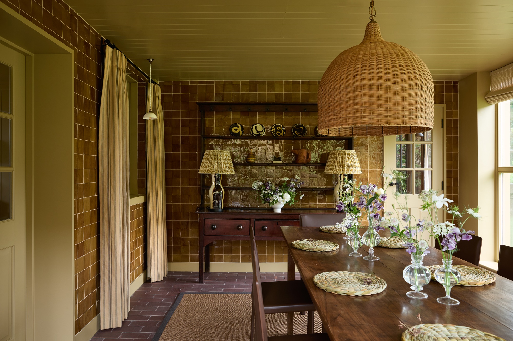a dining room with a dresser, table, curtains and a zellige tiled wall