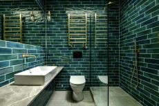 An example of green bathroom ideas showing a bathroom with green wall tiles and brass fixtures and fittings with a glass shower door