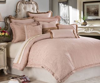 Pink sheets and shams on a bed against a white wall.