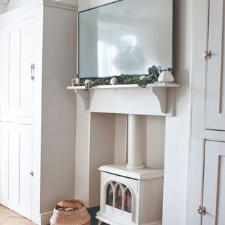 A white dining room with storage cabinets and wood burning stove with a TV placed above it