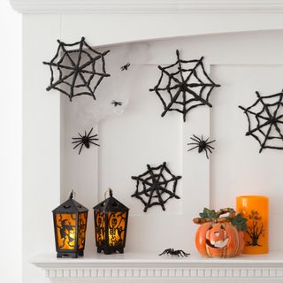 White mantlepiece decorated for Halloween with spiders, cobwebs, lanterns and pumpkin