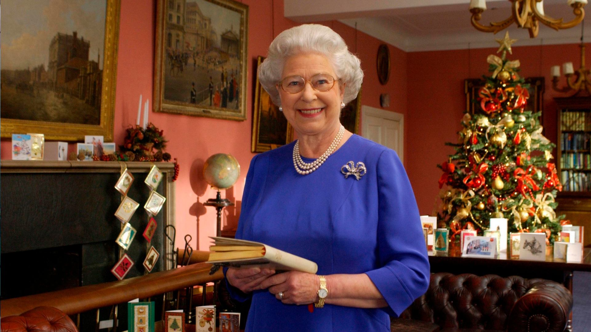 Queen Elizabeth wearing a blue dress standing in front of a Christmas tree