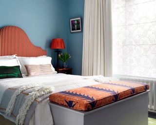 Bedroom with striped upholstered headboard, blanket box and blue walls