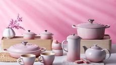 A set of pink Le Creuset cookware against a pink background.