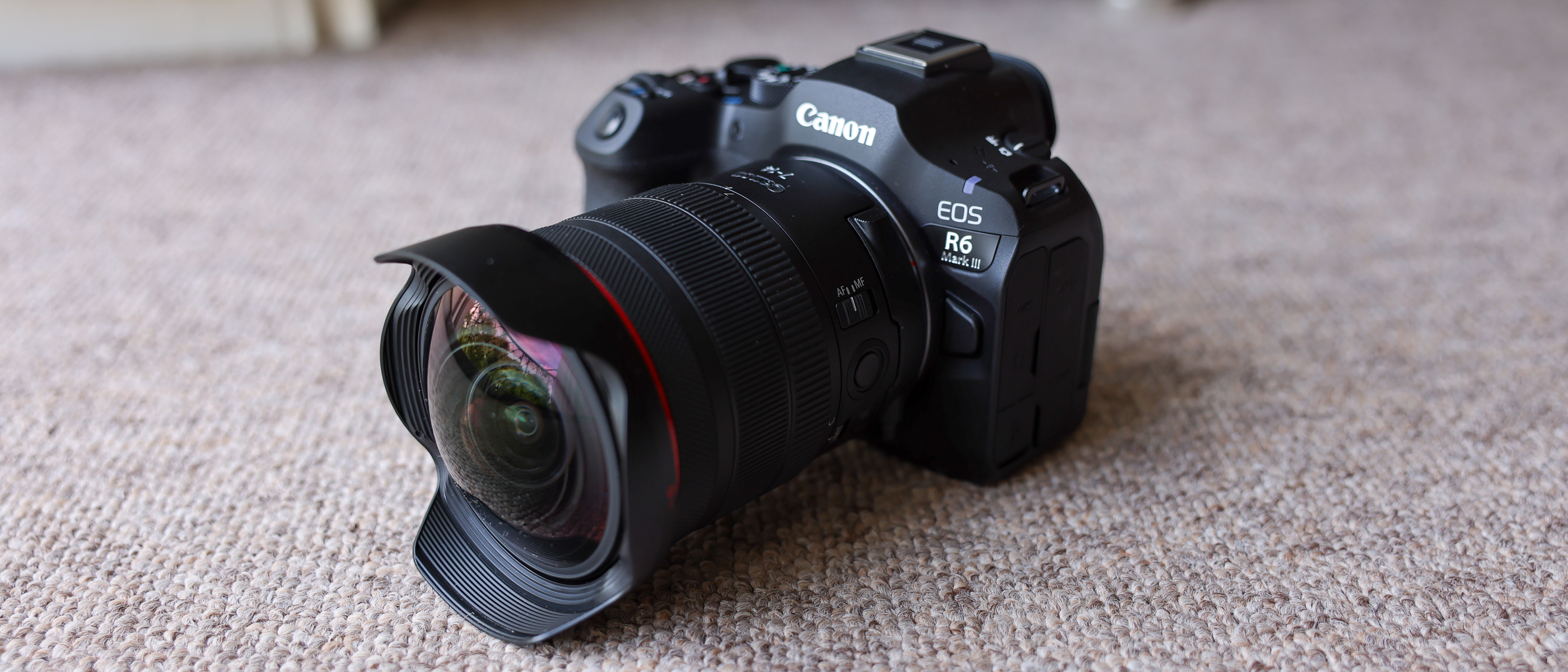 The Canon EOS R6 III with the Canon RF 7-14mm f/2.8-3.5L fisheye lens attached, on a brown carpet.