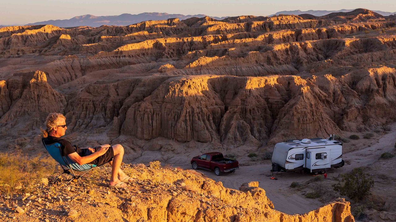 Man lounging on a hill at sunset in the badlands of Anza-Borrego Desert State Park in California. Pickup truck and camper below.