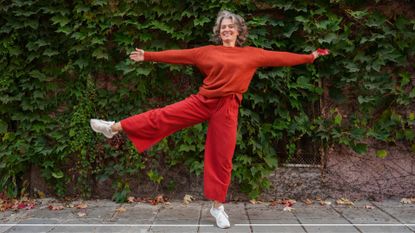 Woman smiling, holding arms and legs out in back garden, wearing bright matching activewear, representing how to lower your biological age through movement