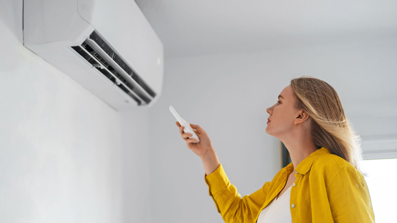 woman using remote control on wall mounted air conditioner