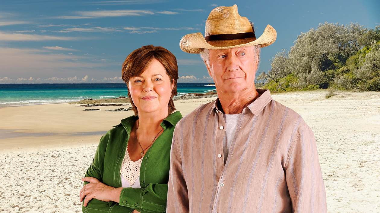 Darby and Joan standing with a beach behind them
