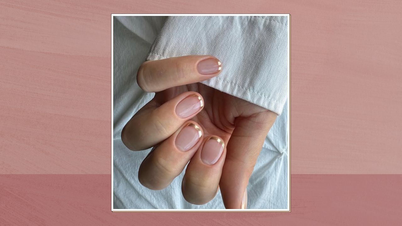 Close up of woman&#039;s hand with manicured nails and metallic tips, in a white frame set against a dark pink watercolour-style background