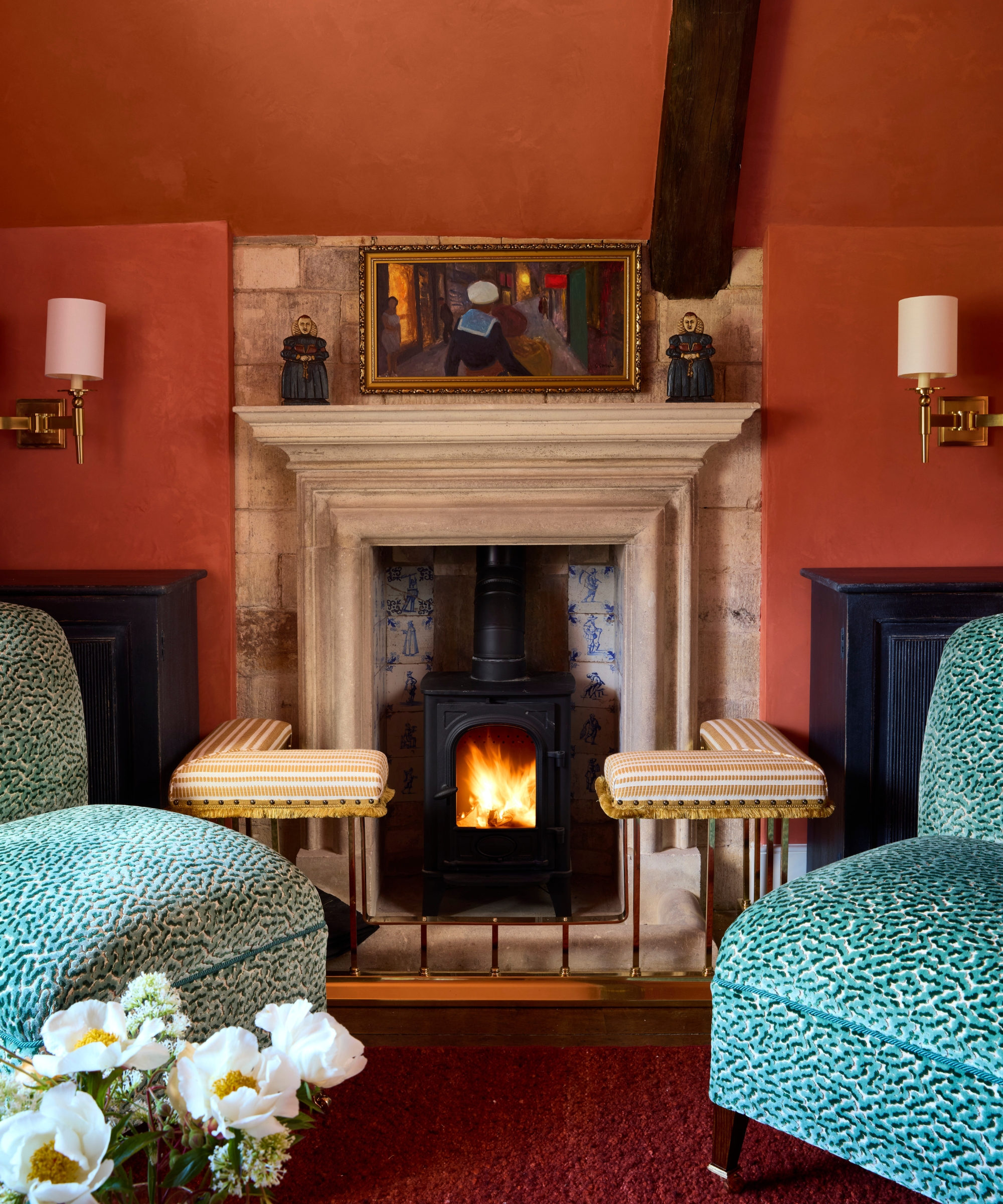 Terracotta living room with textured plaster walls, stone fireplace, wood-burning stove, turquoise armchairs, and brass wall sconces.