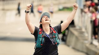 Woman raising her hands in the air with happiness wearing hydration vest after finishing a marathon