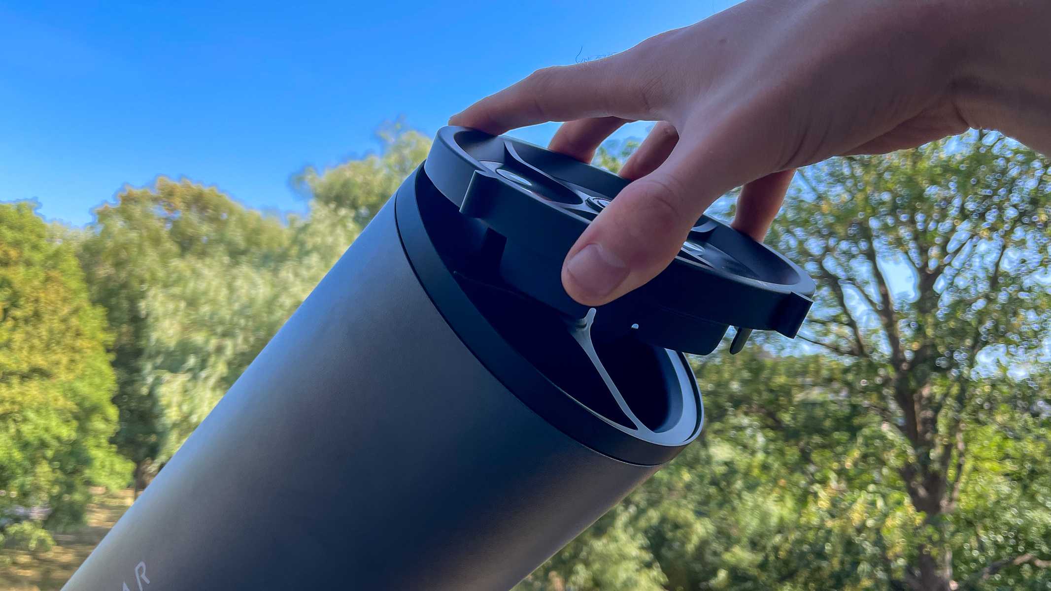 A hand attaching the solar filter to a Unistellar eVscope 2 with trees in the background.