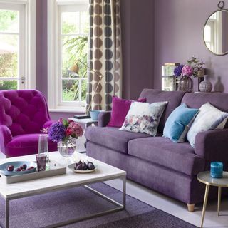 A purple room with purple sofas, a purple rug and a round wall mirror