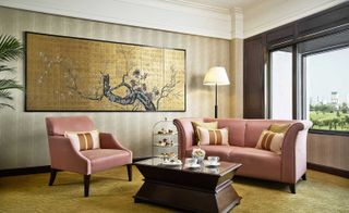 Seating area with pink sofa and chair, wooden coffee table with cake stand, and oriental artwork