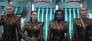 A man and three women dressed in brown and bronze sci-fi uniforms.