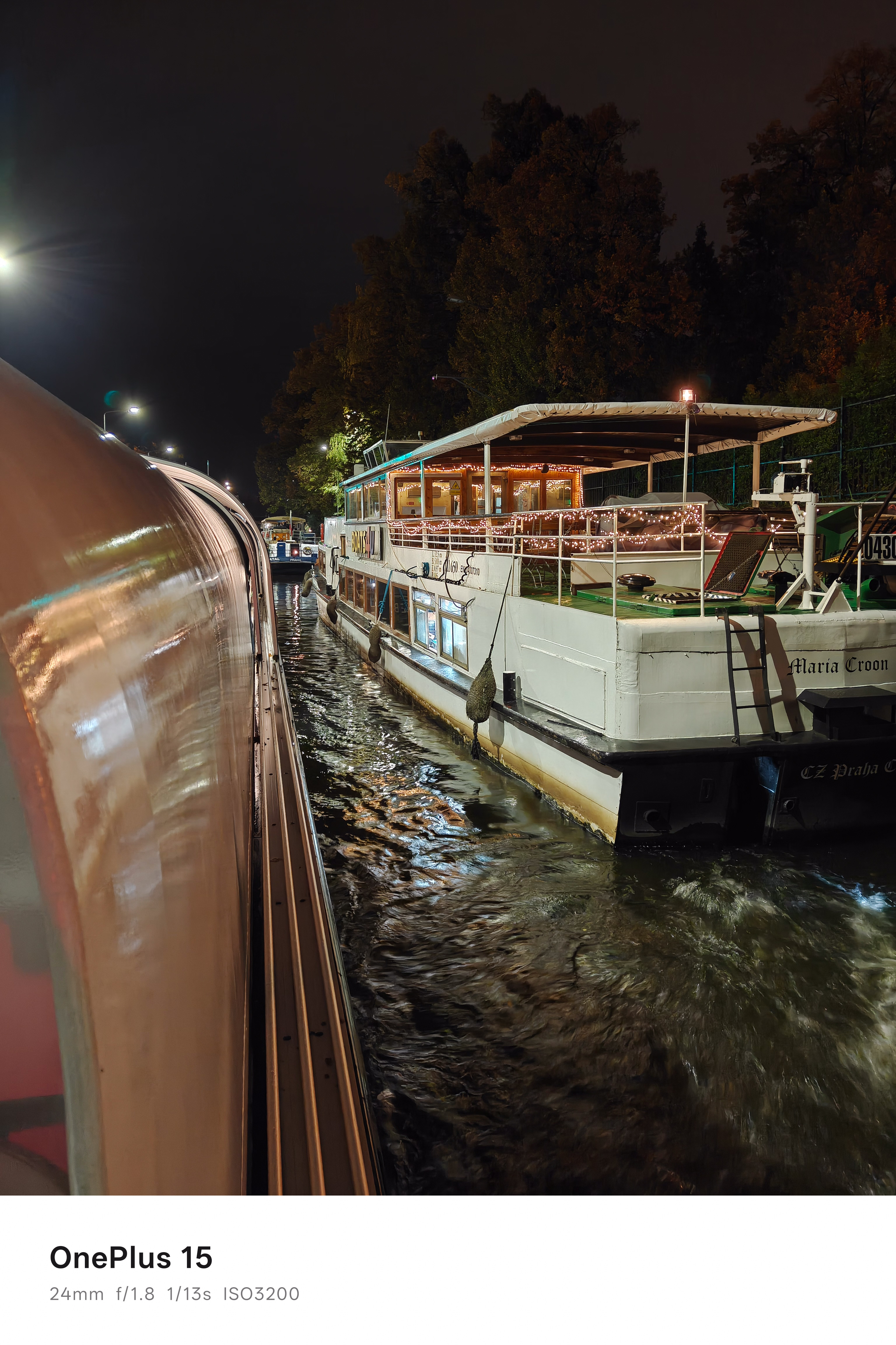 Two boats lit up at night passing each other on a narrow river